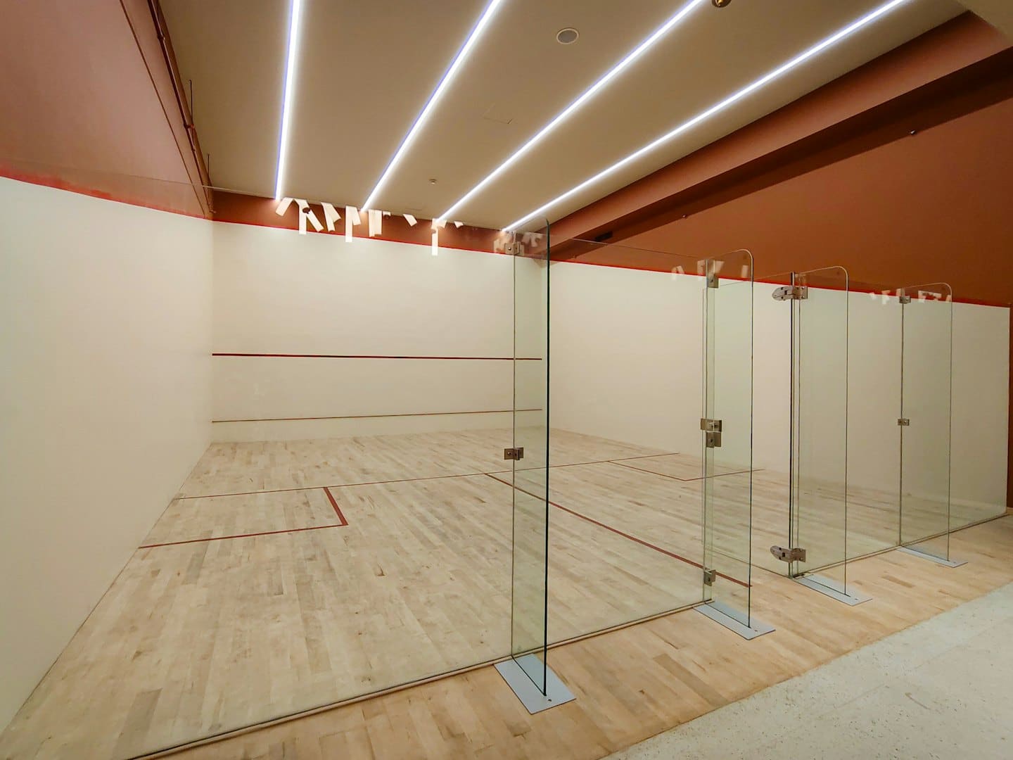 Campo da squash moderno e vuoto con pavimenti in legno e pareti di vetro.